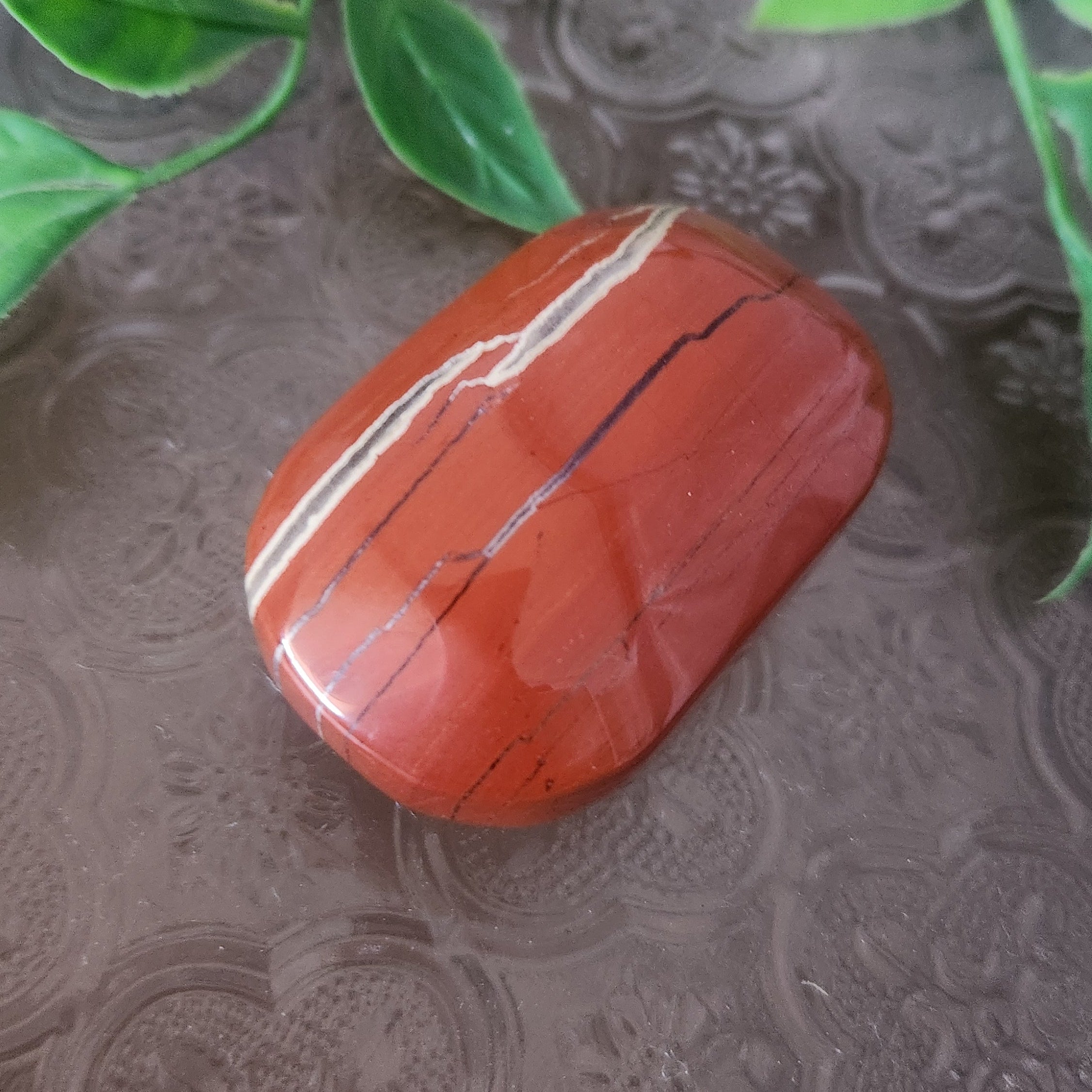 Polished red jasper crystal palmstone showing earthy red tones and white veining