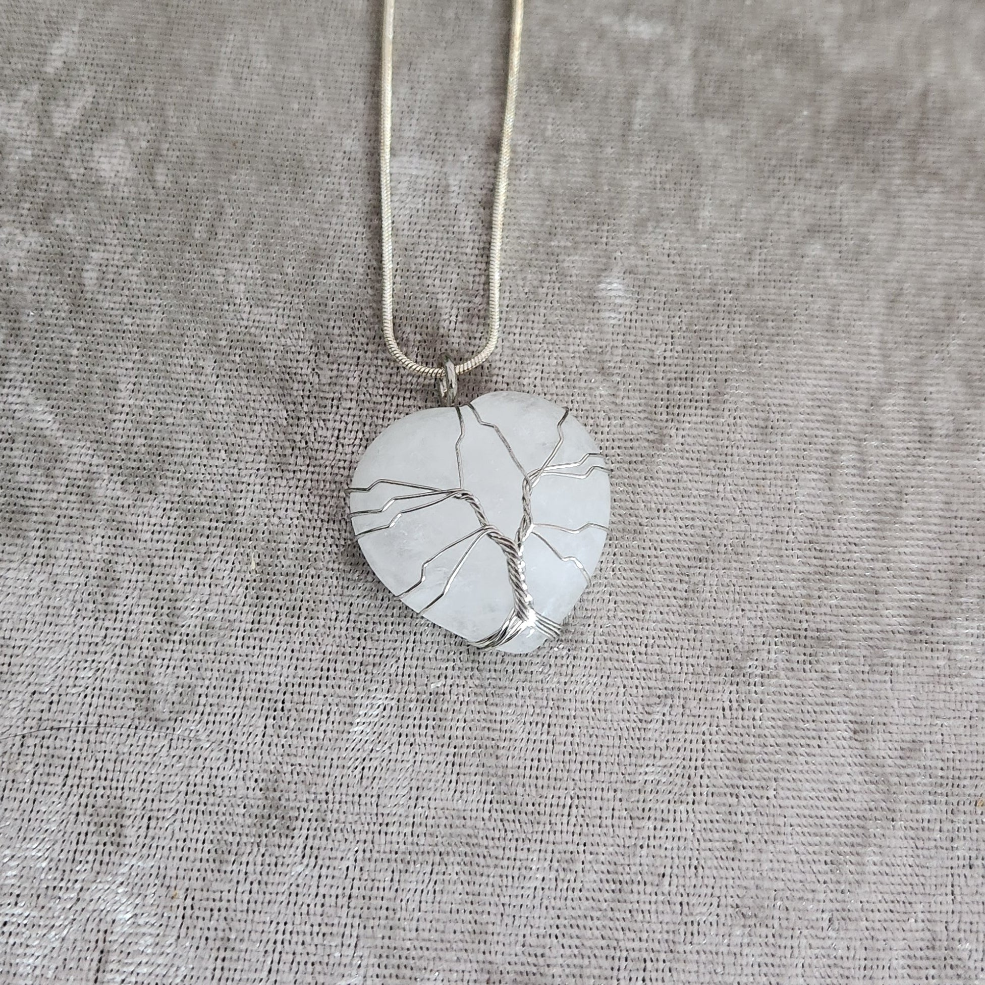Clear quartz heart necklace with silver wire wrap on neutral fabric