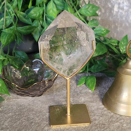 Clear quartz with rutile inclusion crystal elegantly displayed on gold stand, highlighting natural textures and clarity.