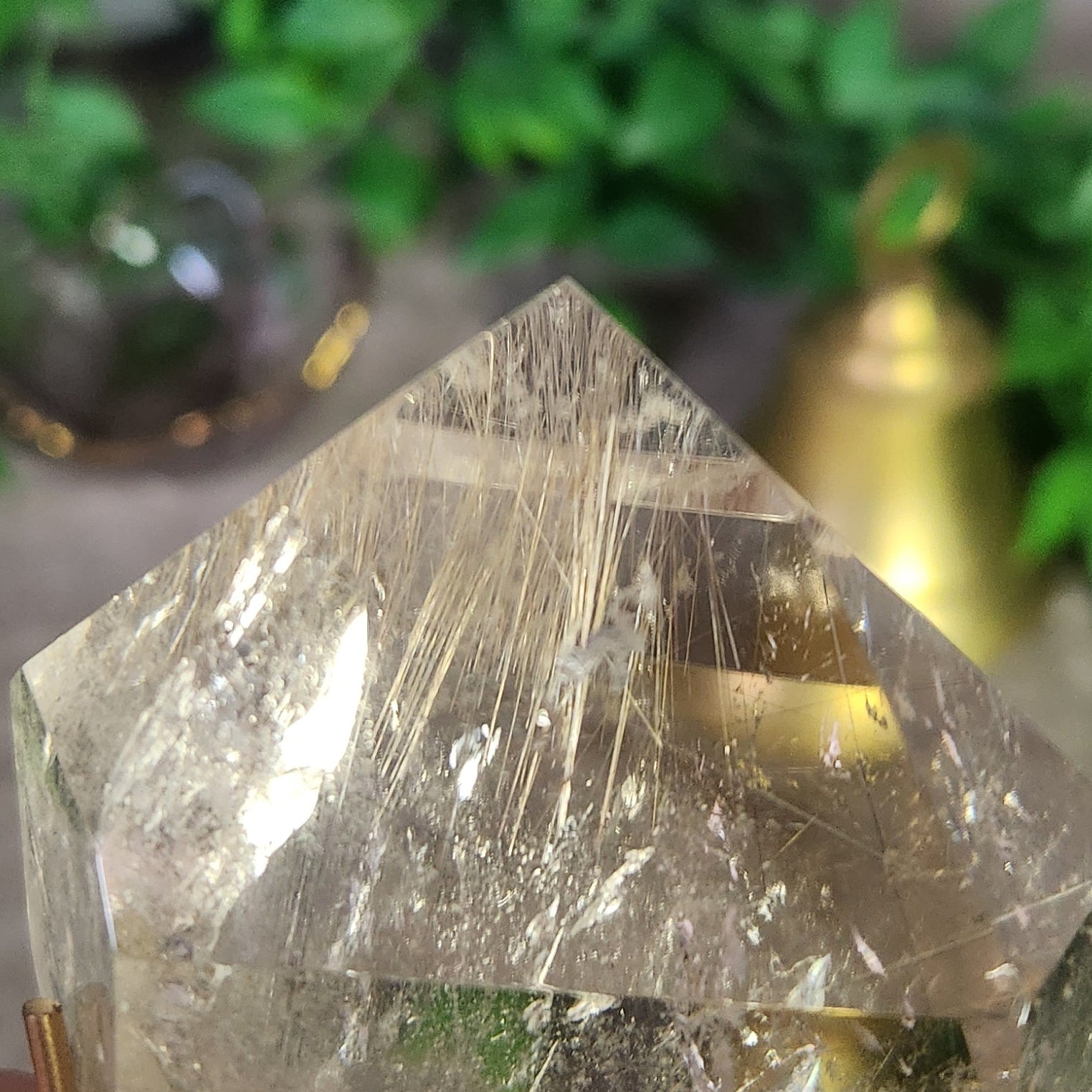 Close-up of Brazilian clear quartz point with shimmering golden rutile threads and stand, capturing light reflections.