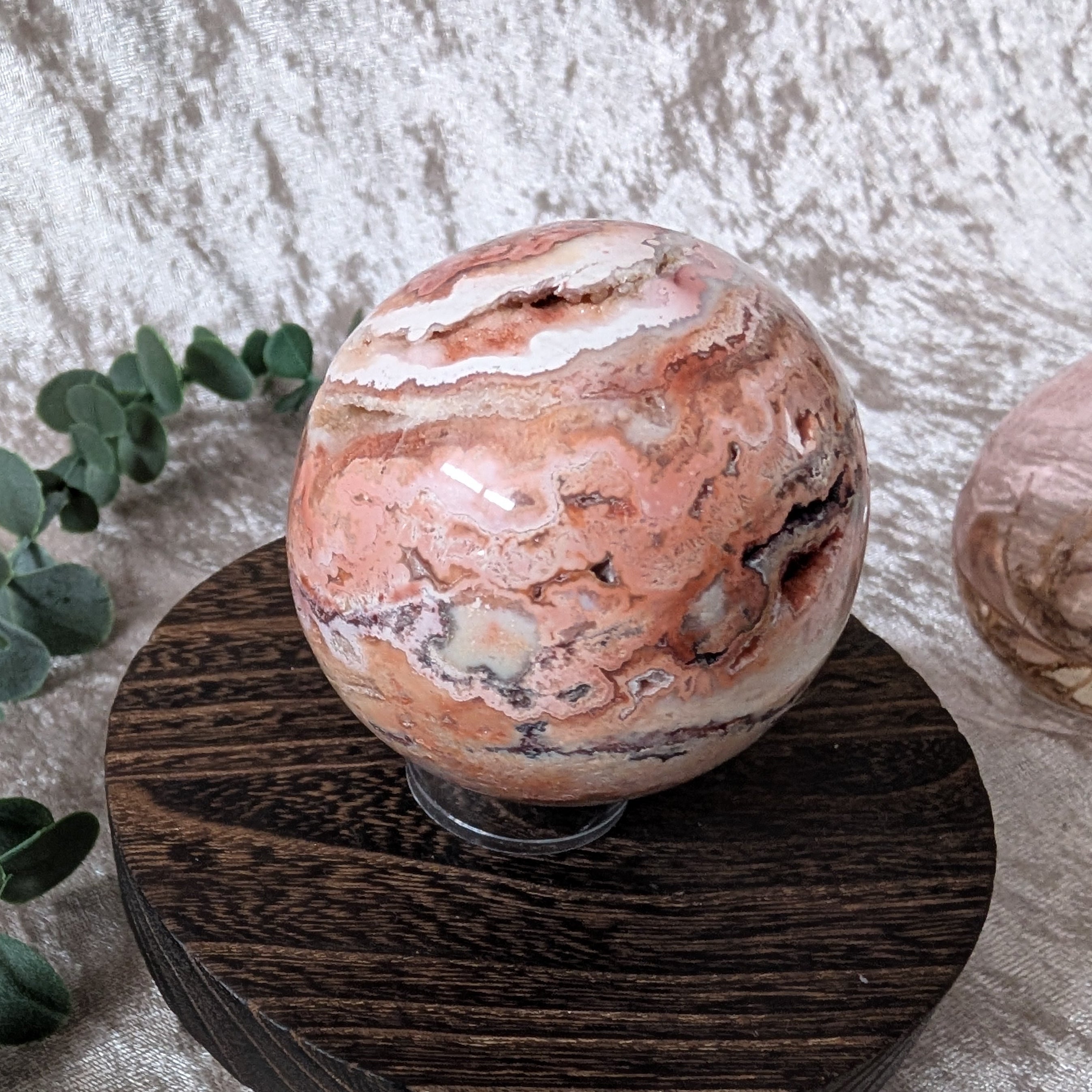 Crazy lace agate sphere with peach, cream and brown banded patterns displayed on wooden stand