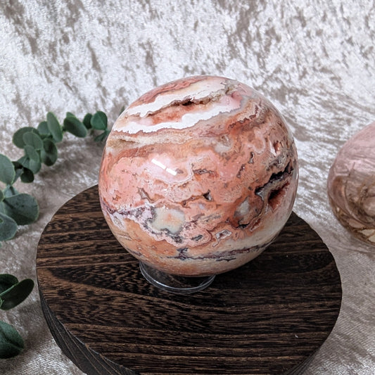 Crazy lace agate sphere with peach, cream and brown banded patterns displayed on wooden stand