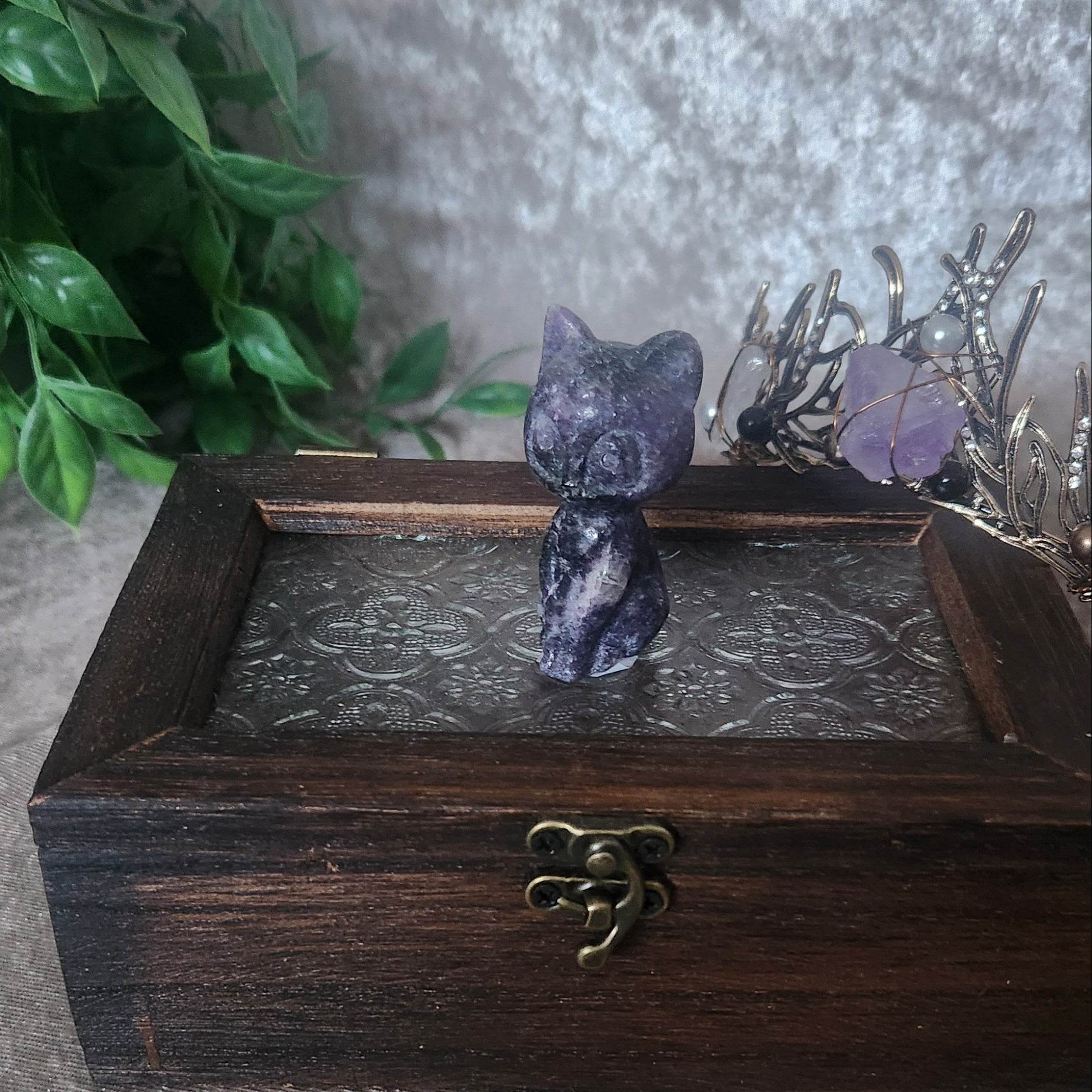 Purple lepidolite crystal cat carving with natural black and white inclusions displayed on a wooden box