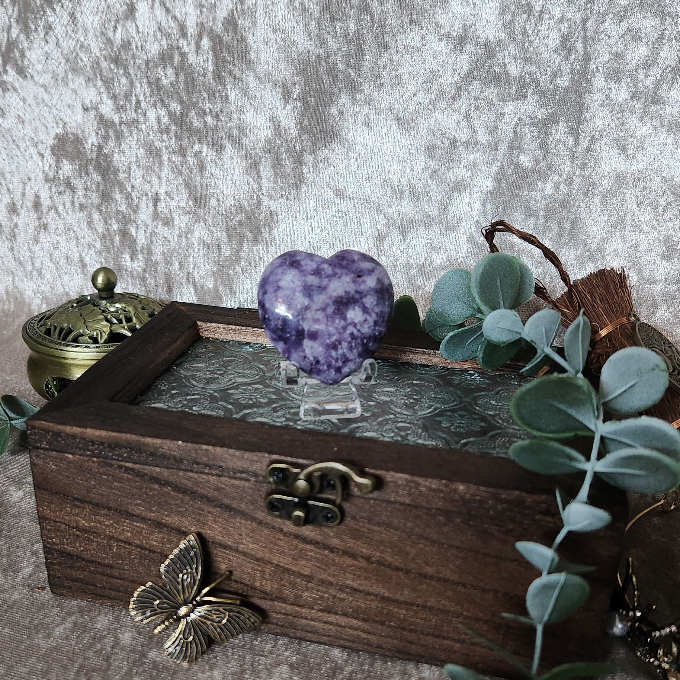 Polished lepidolite heart crystal on glass stand styled on rustic wooden box with soft botanical accents