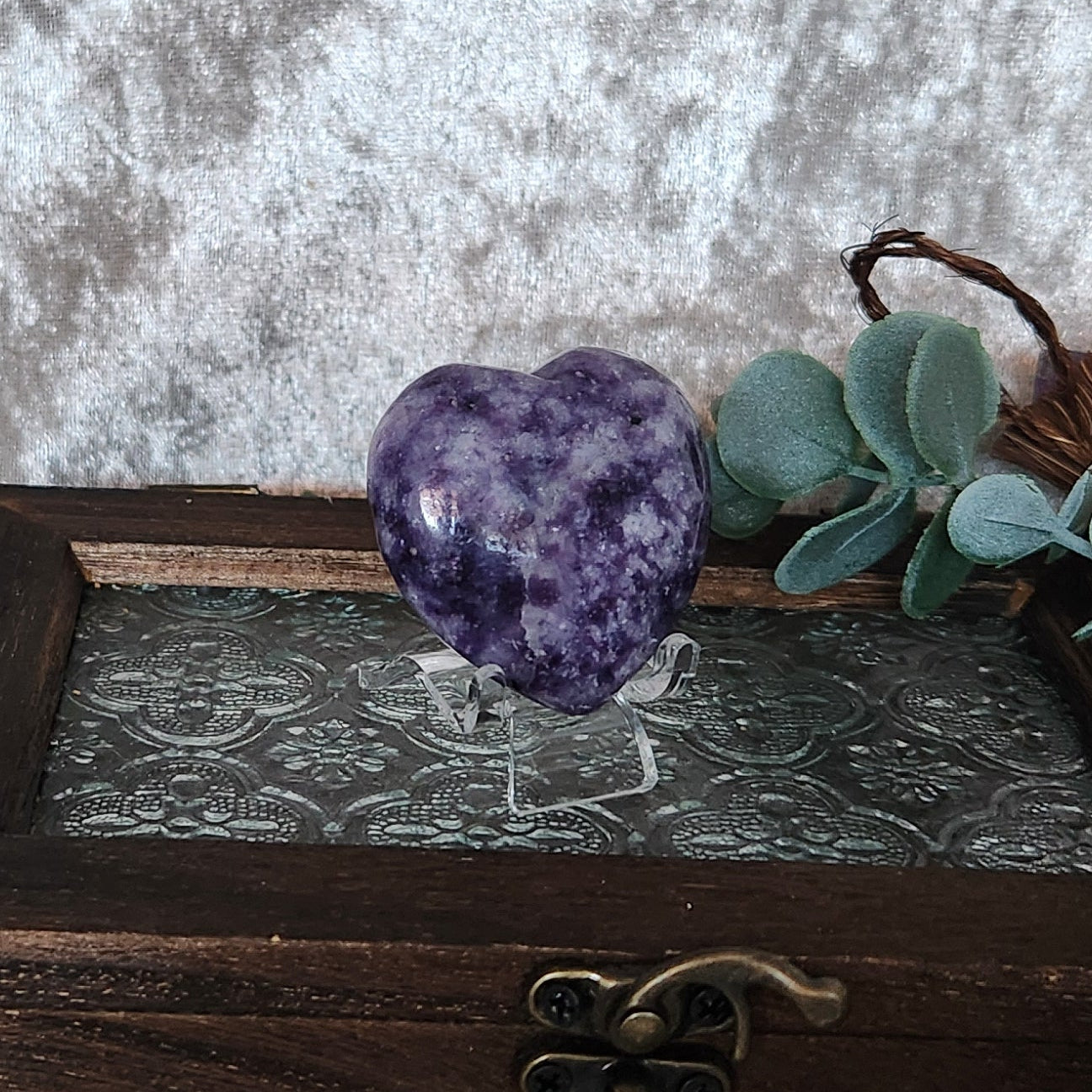 Lepidolite crystal heart photographed on decorative wooden box with greenery and mystical props