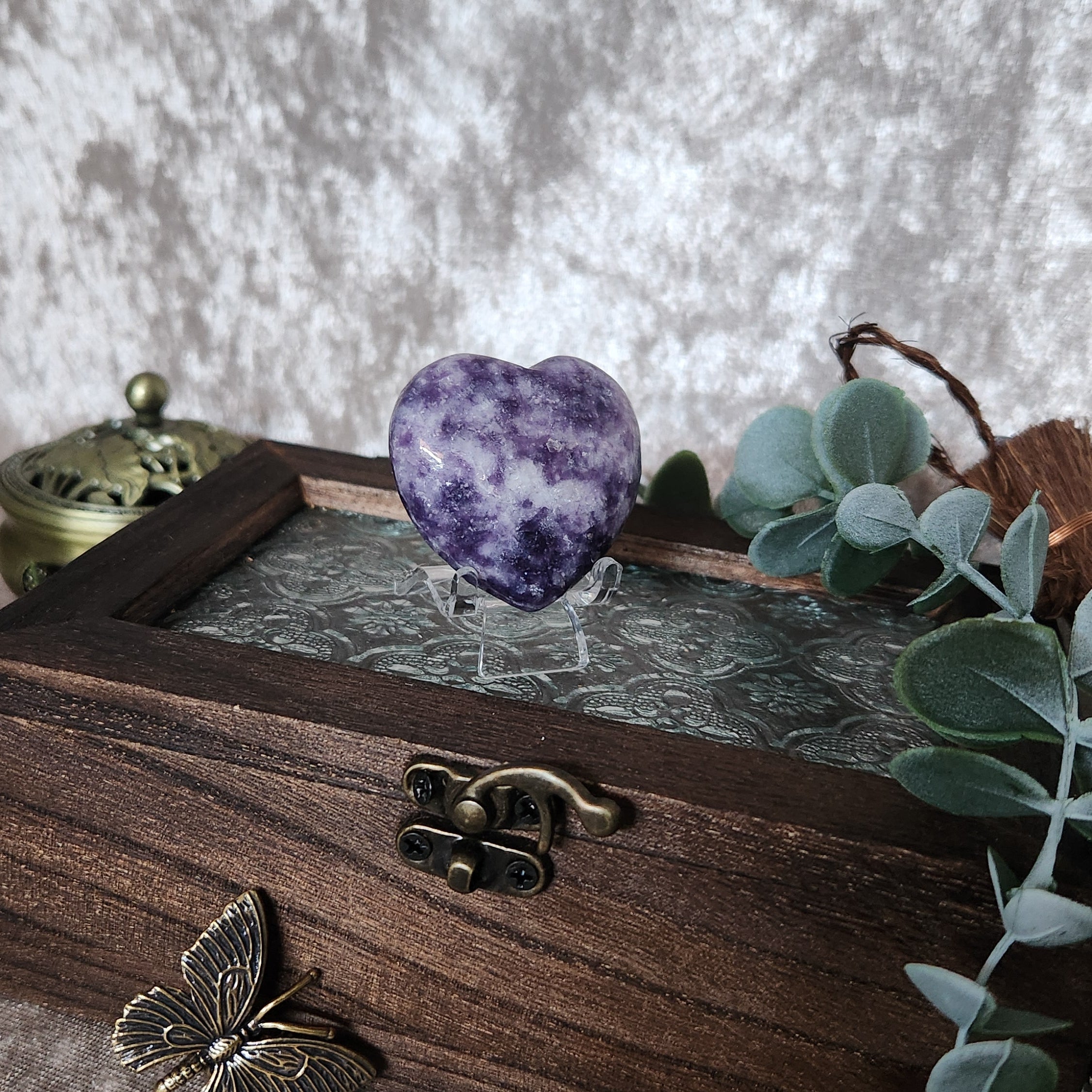 Soft purple lepidolite heart crystal showcased on small stand with boho styled background and foliage