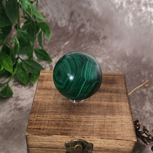 Polished malachite sphere with deep green banding displayed on wooden box