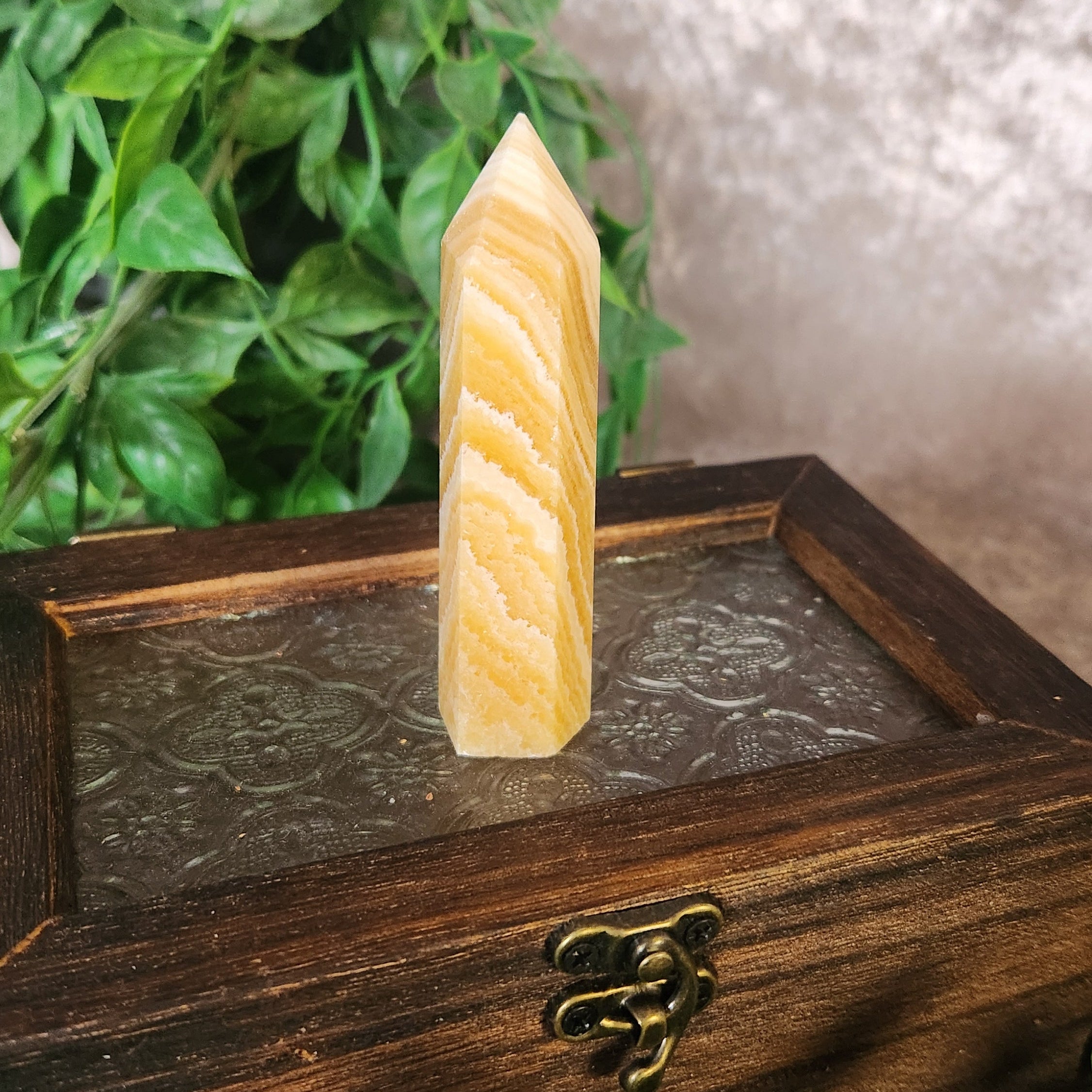 Orange banded calcite tower with warm orange and cream layered bands displayed upright on a wooden box