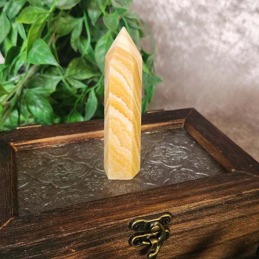 Orange banded calcite tower with warm orange and cream layered bands displayed upright on a wooden box