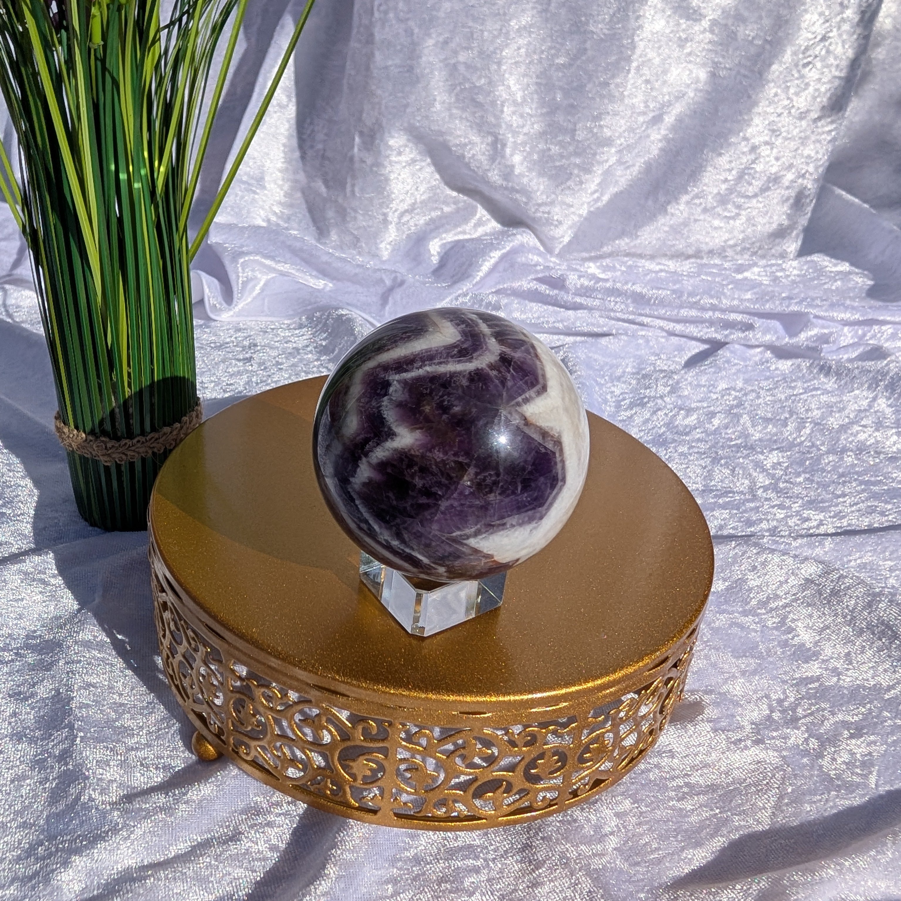 Dream Amethyst displayed in natural light on golden stand and soft white velvet background