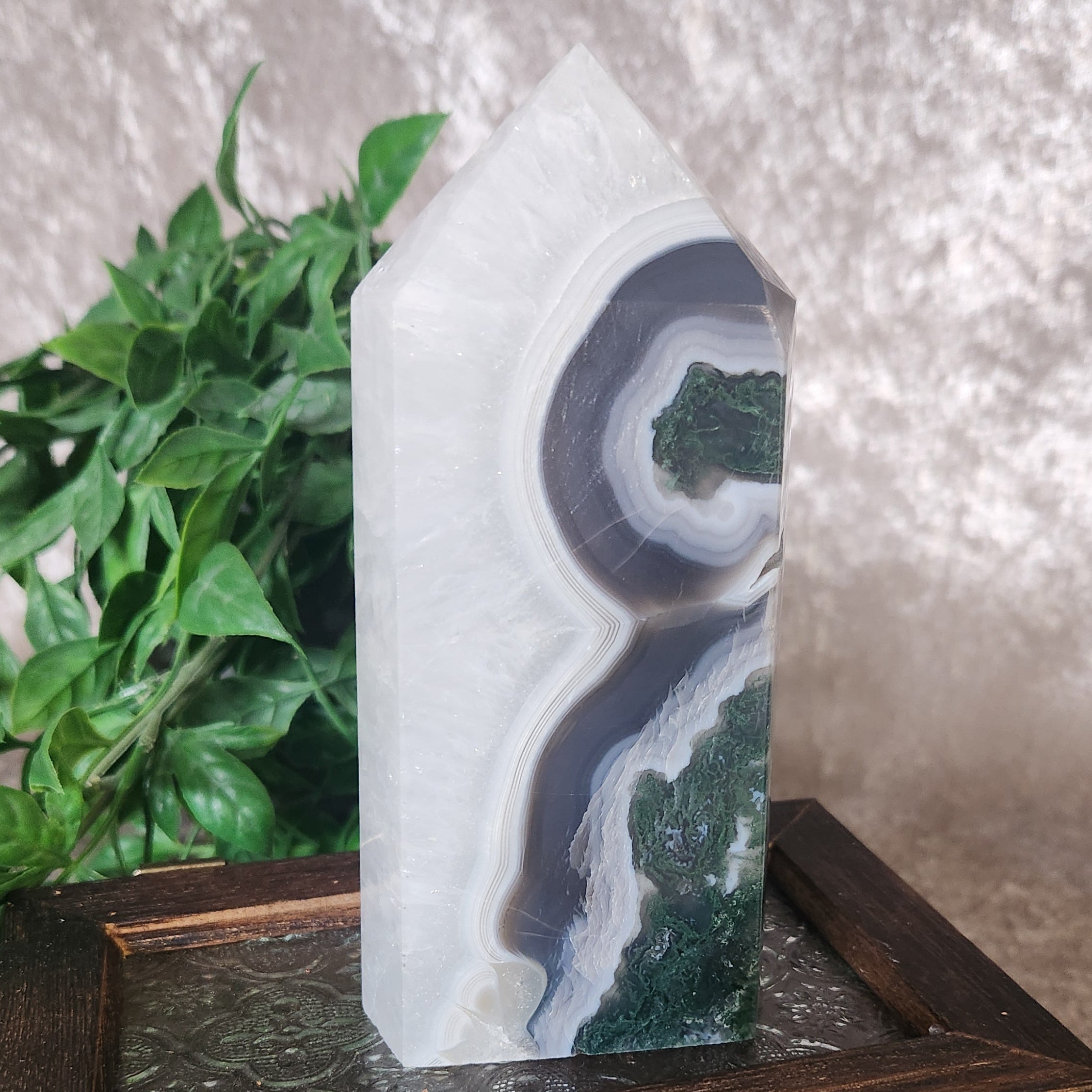 Parallax moss agate tower with layered grey and white banding and deep green moss inclusions displayed on a wooden box