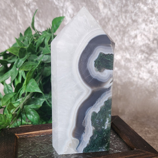Parallax moss agate tower with layered grey and white banding and deep green moss inclusions displayed on a wooden box