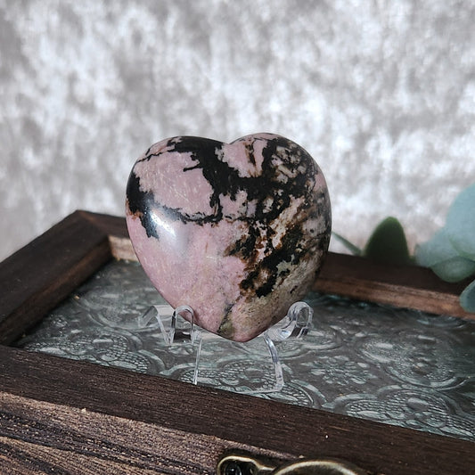 Rhodonite heart crystal on clear stand displayed on wooden box with botanical styling