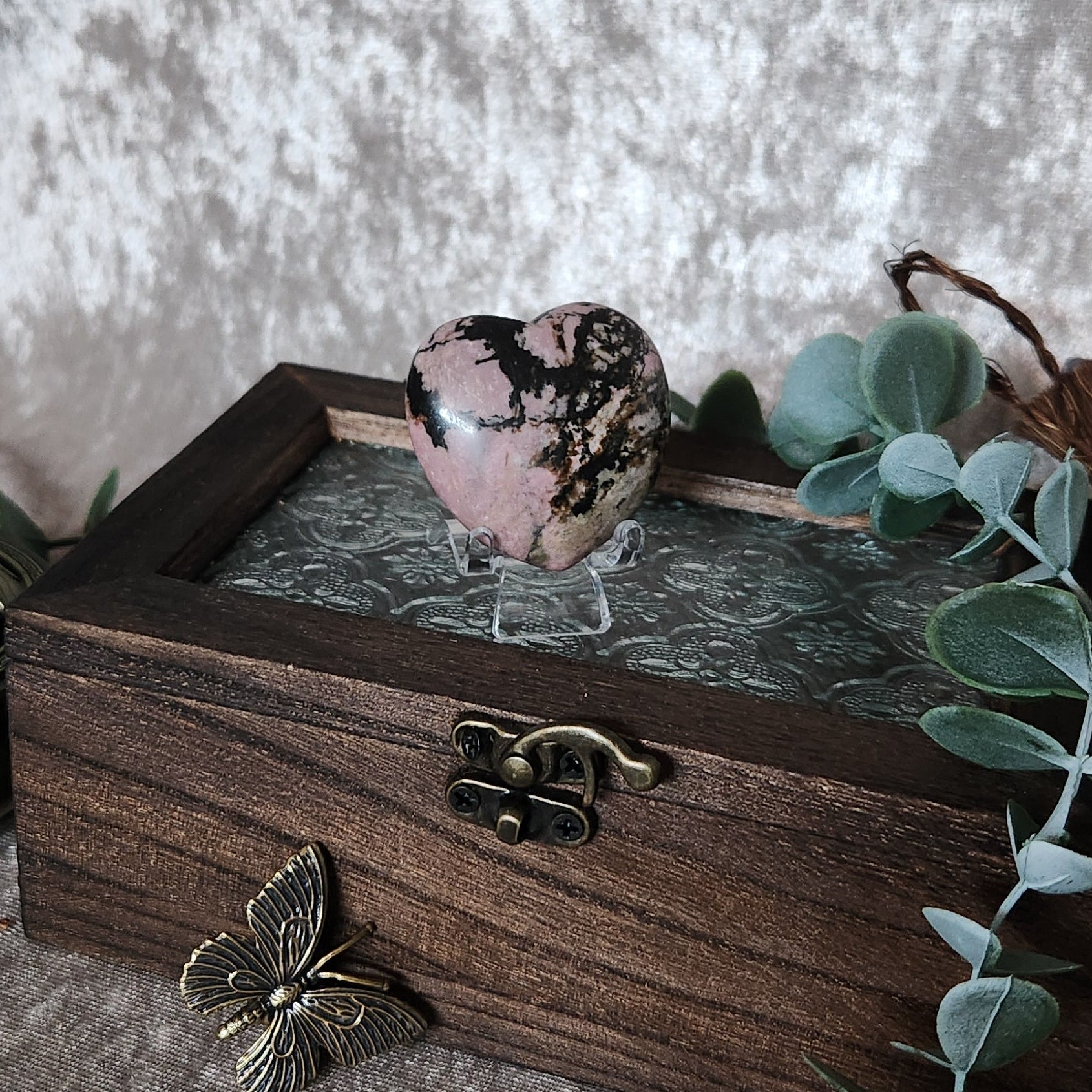 Polished rhodonite heart gemstone with black veining displayed on rustic wooden chest