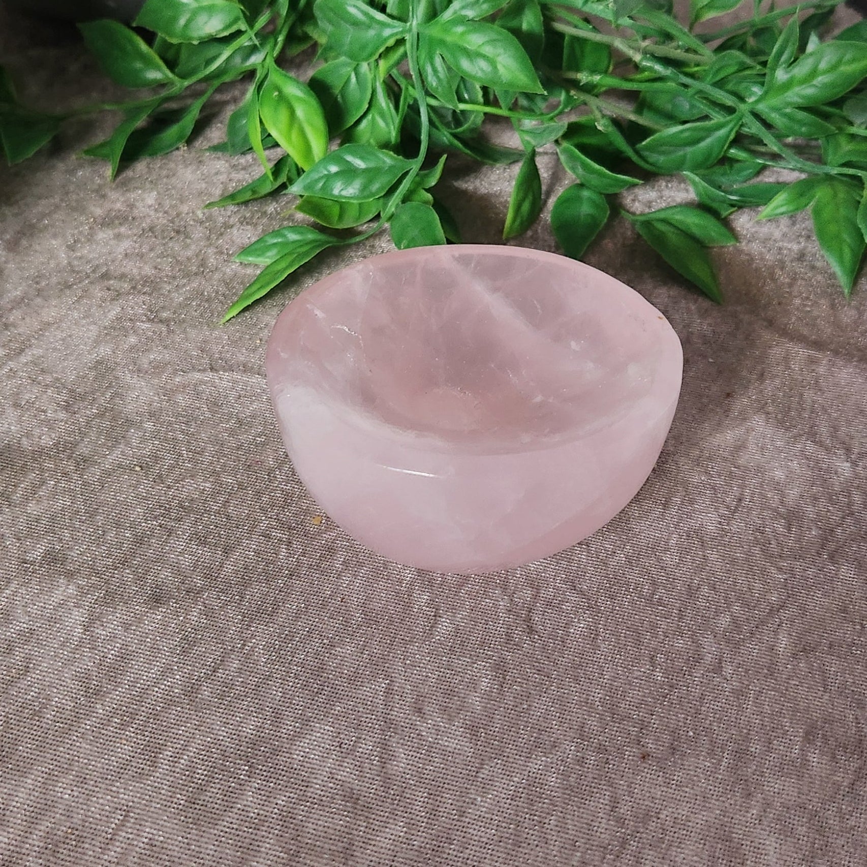 Polished rose quartz bowl with soft pink tones shown from above on neutral fabric background