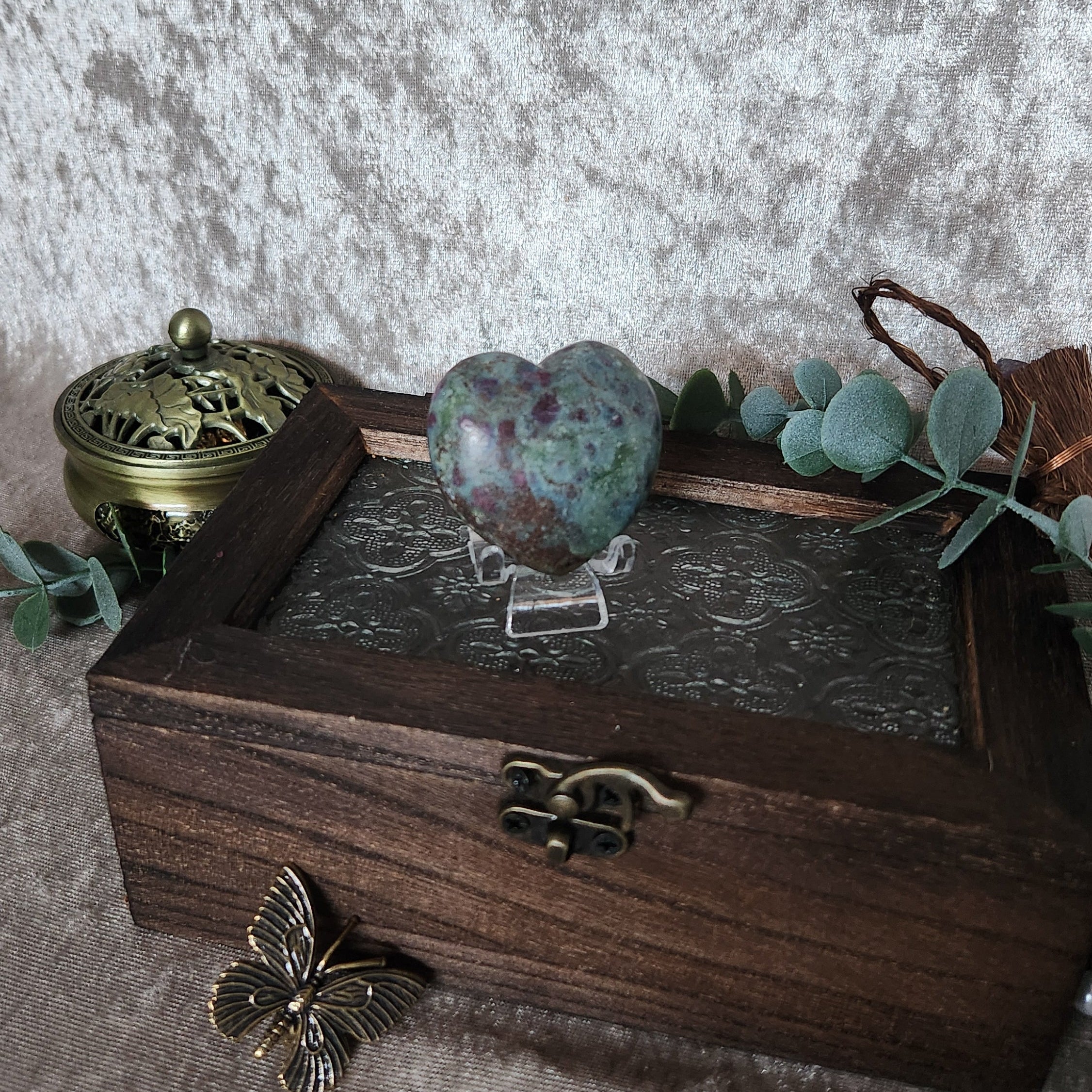 Natural ruby in kyanite heart crystal photographed on decorative wooden chest with greenery and mystical props