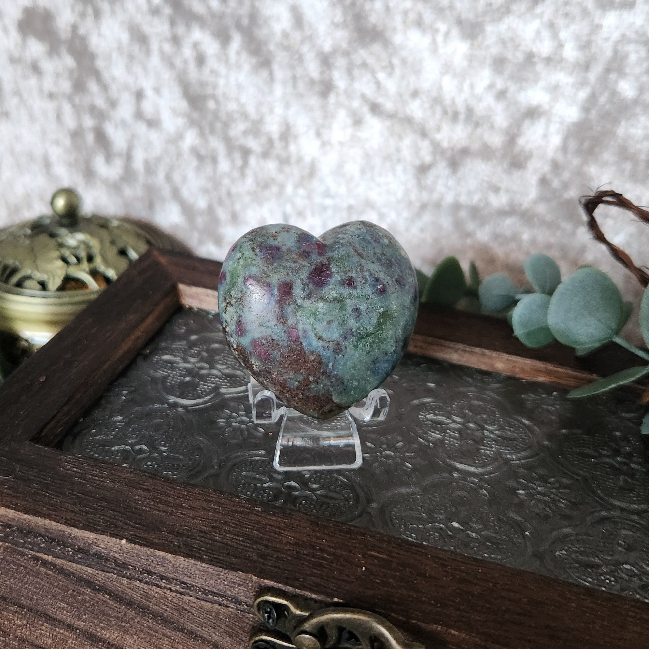 Blue and red ruby in kyanite heart crystal showcased on small stand with boho styled background