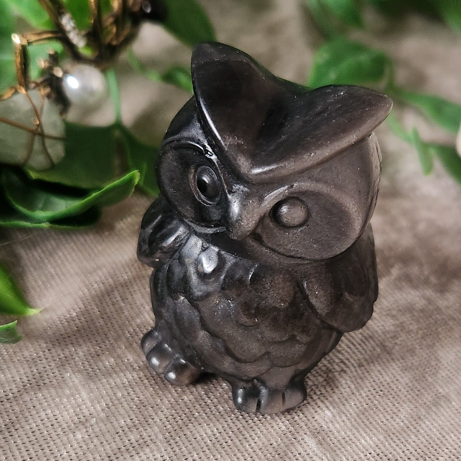 Small silver obsidian owl figurine displayed with greenery