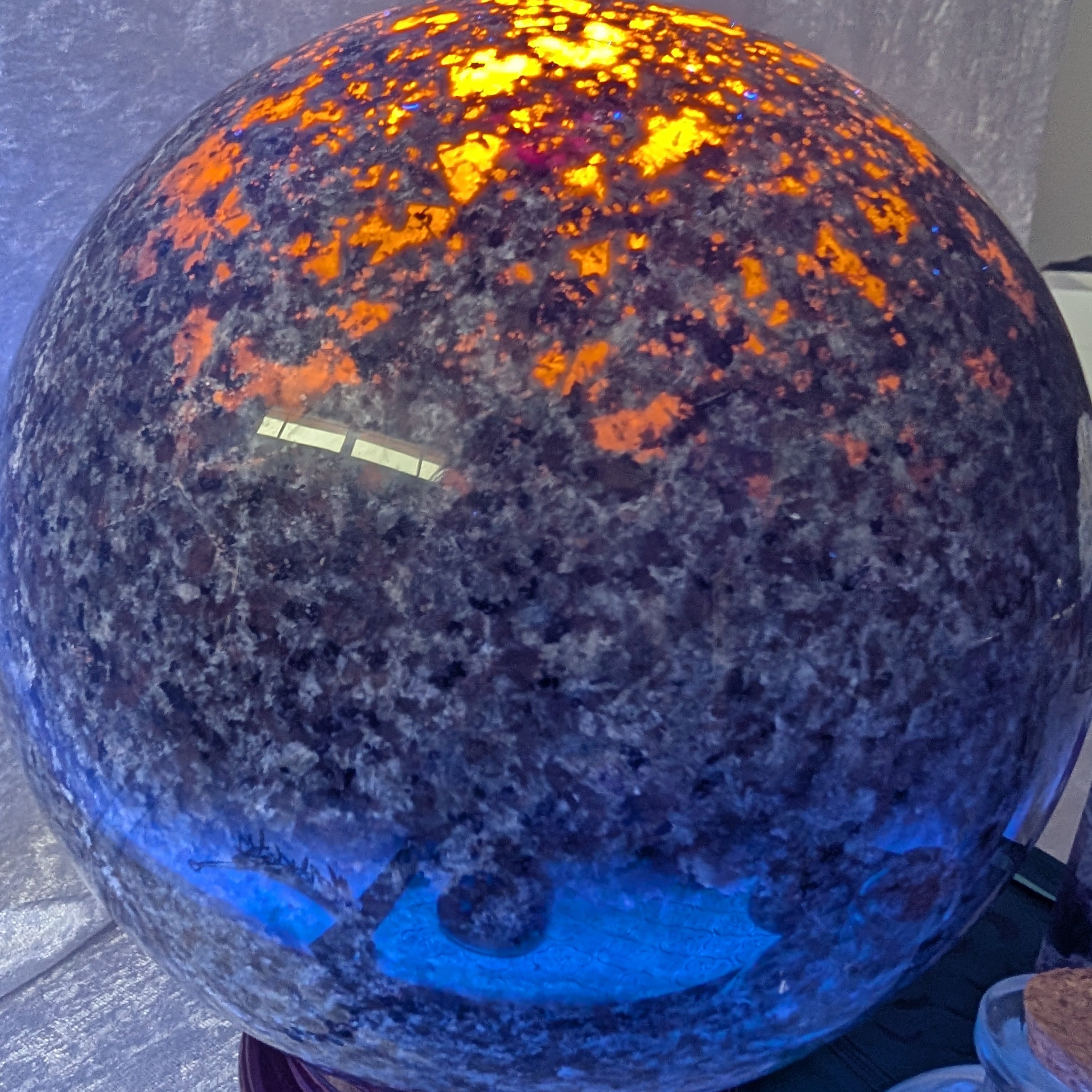 Close-up of Yooperlite Sphere glowing under UV light, showing vivid orange spark-like fluorescence across the surface.
