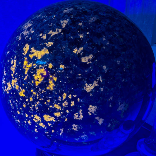 Yooperlite Sphere under UV light glowing with bright orange fluorescence, highlighting its unique sodalite-rich pattern.