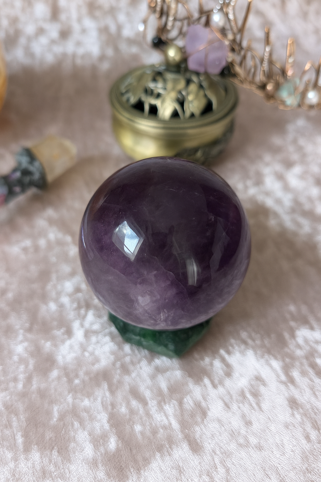 Polished Amethyst crystal sphere with deep violet tones on green stand, displayed on silver velvet.