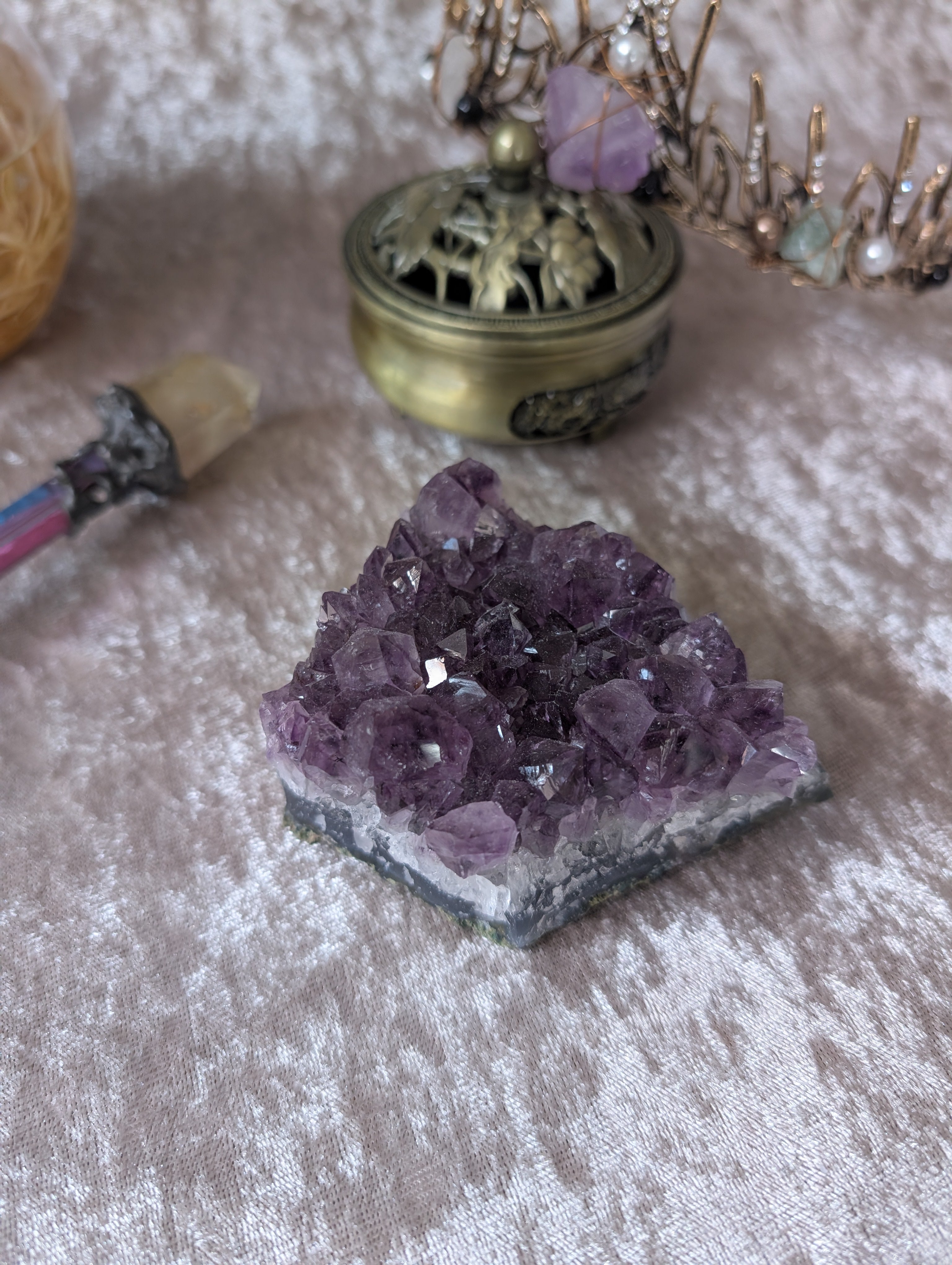 Amethyst crystal cluster on matrix with sparkling violet points, displayed on silver velvet fabric.