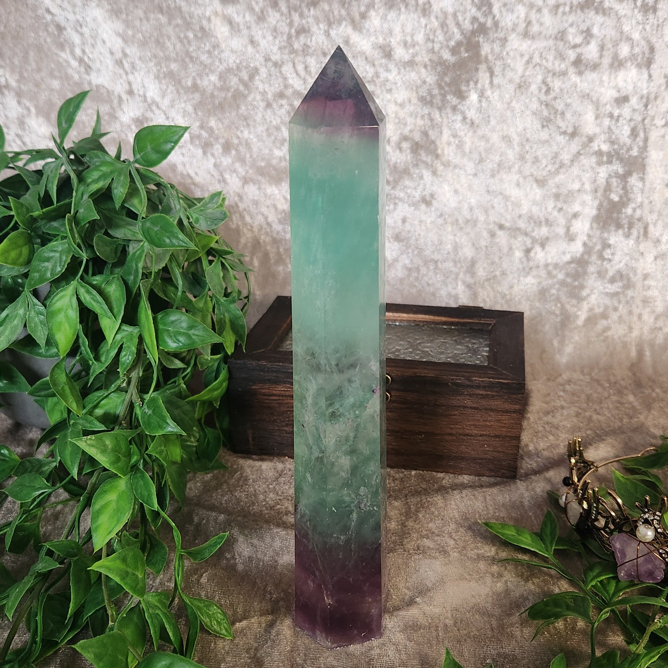 Tall rainbow fluorite crystal tower with green and purple colour zoning displayed among greenery