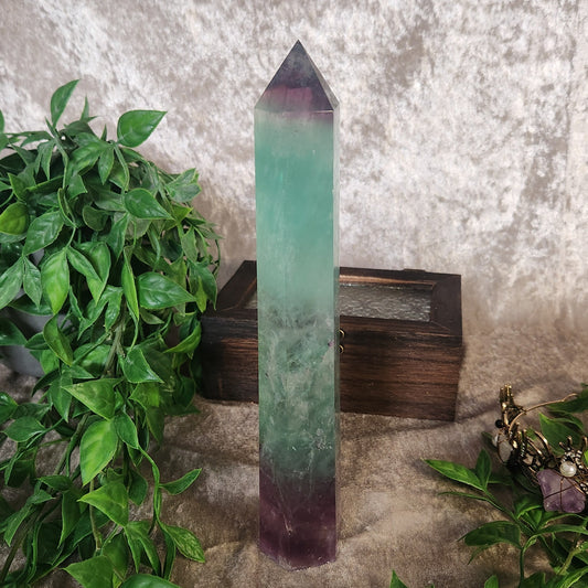Tall rainbow fluorite crystal tower with green and purple colour zoning displayed among greenery